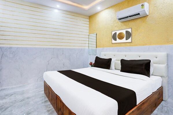 A modern bedroom with a marble floor, a white bed with black and white bedding, a gold accent wall, and an air conditioning unit.
