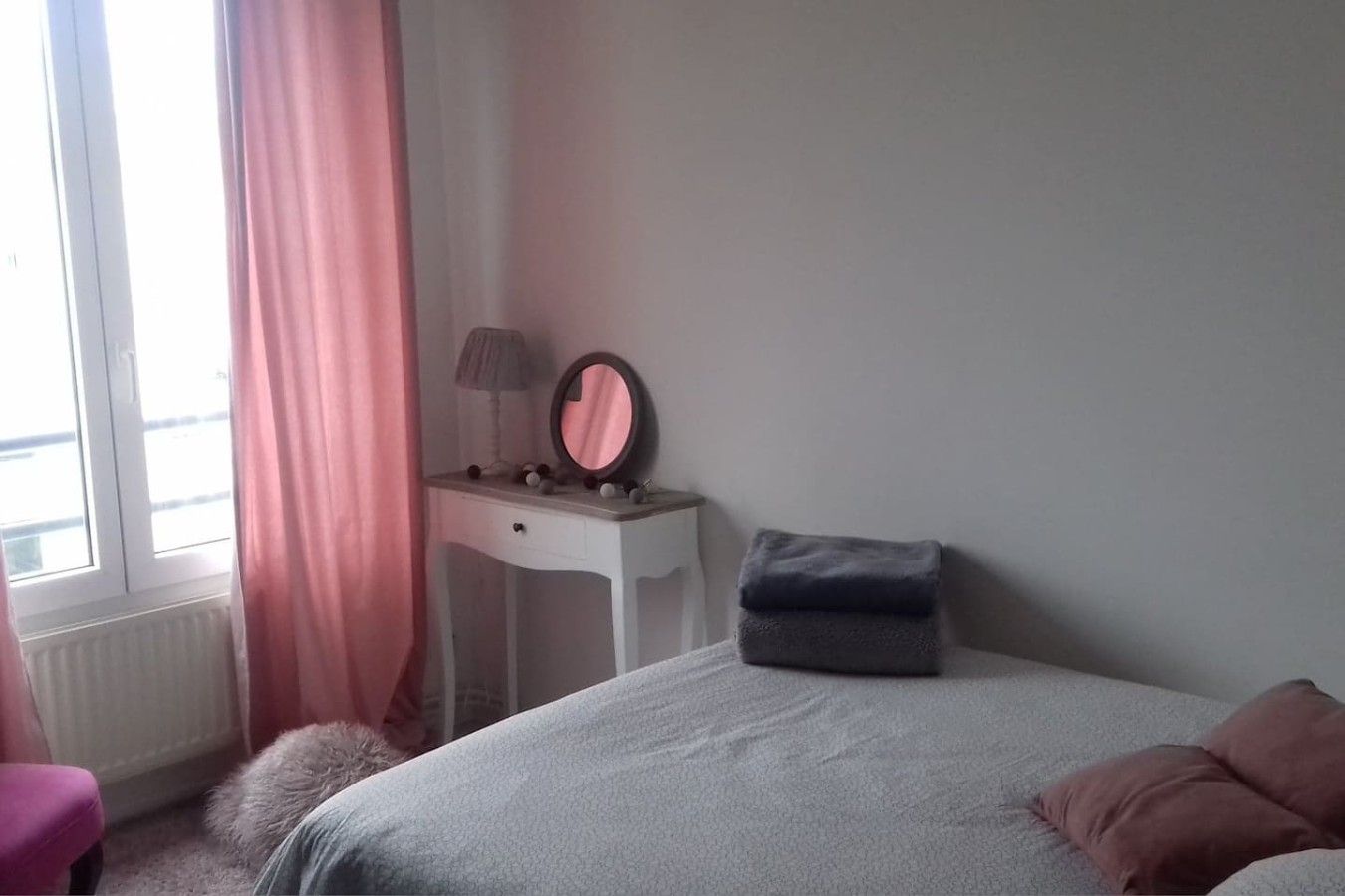 Une chambre à coucher avec un lit, une table de chevet avec une lampe, un miroir et une fenêtre avec des rideaux.