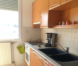 A kitchen with wooden cabinets, a double sink, a coffee maker, and a window with blinds.