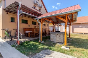 A covered outdoor seating area with a stone bench and a table, adjacent to a building with air conditioning units.