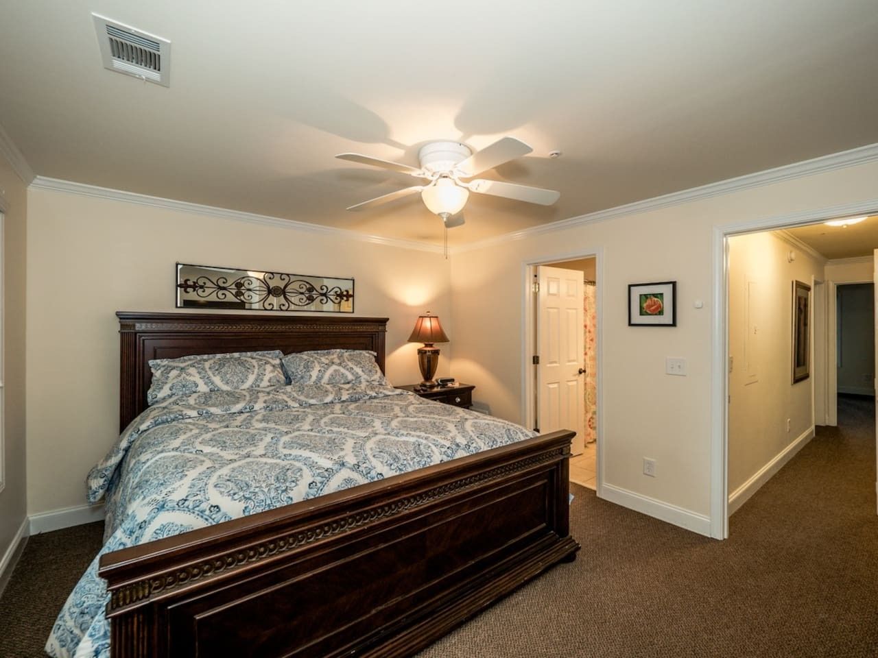 A bedroom with a bed, a ceiling fan, a nightstand, and a door leading to another room.