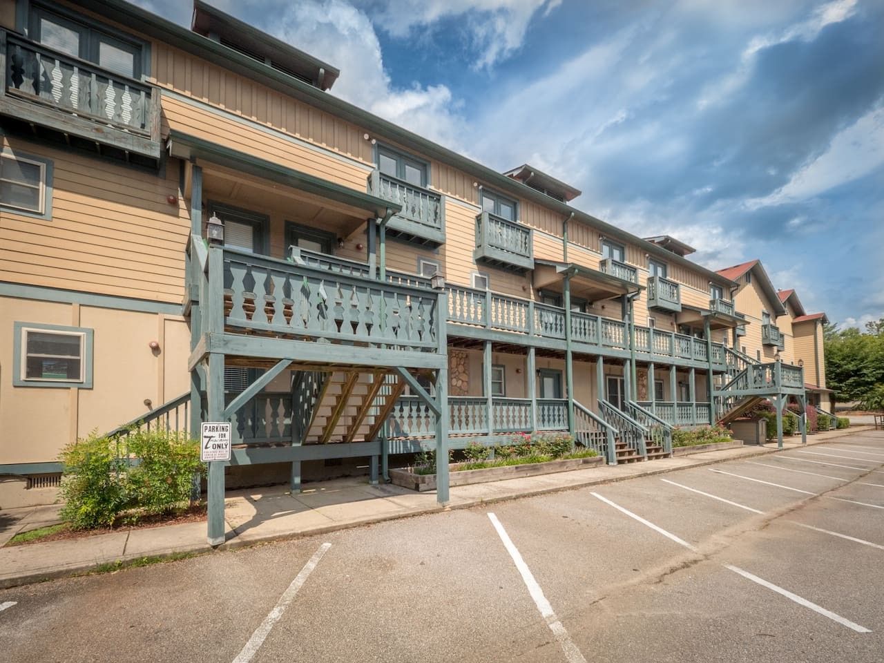 A multi-story hotel with balconies, a parking lot, and a staircase leading to the entrance.