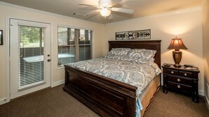 Une chambre à coucher avec un lit, une table de chevet, un ventilateur de plafond et une porte avec des stores.