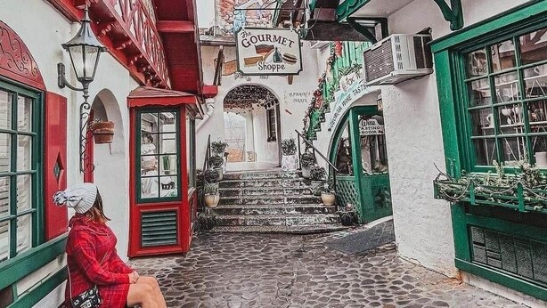 Une ruelle étroite pavée, bordée d’un bâtiment sur lequel on peut voir une enseigne indiquant « The Gourmet Shoppe ».