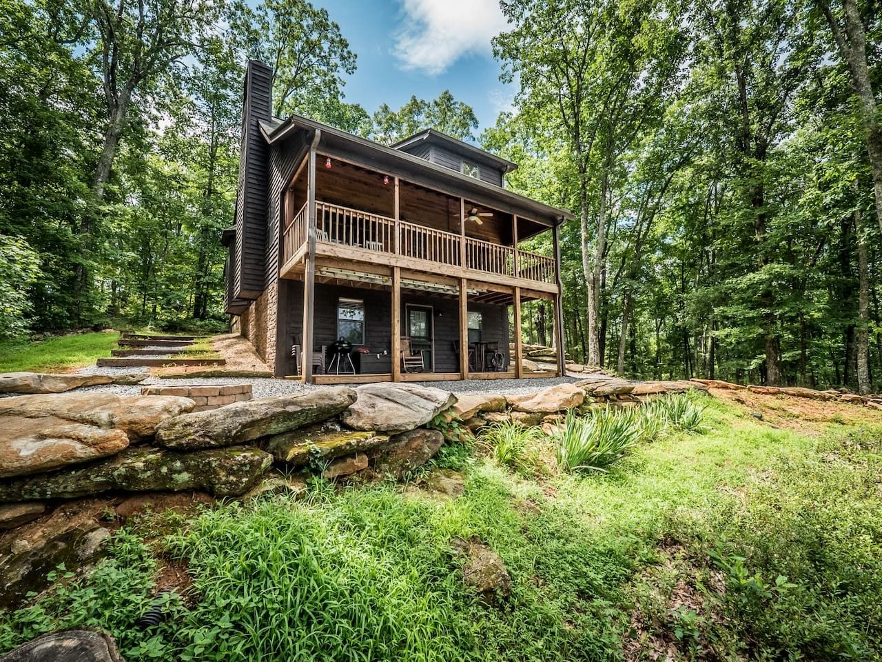 A cabin with a wooden deck and a stone retaining wall.