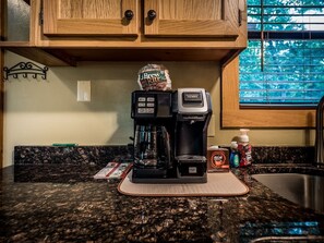 Una cocina con cafetera, dispensador de cápsulas de café y una taza de café sobre la encimera.