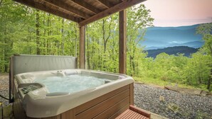 Ein Whirlpool auf einer Holzterrasse mit Blick auf einen Wald und Berge.