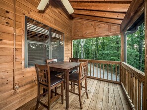 Una terraza de madera con una mesa y sillas, rodeada de paredes y barandilla de madera.