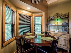 Un comedor con una mesa de madera, cuatro sillas y una zona de cocina con estante y un letrero de neón.