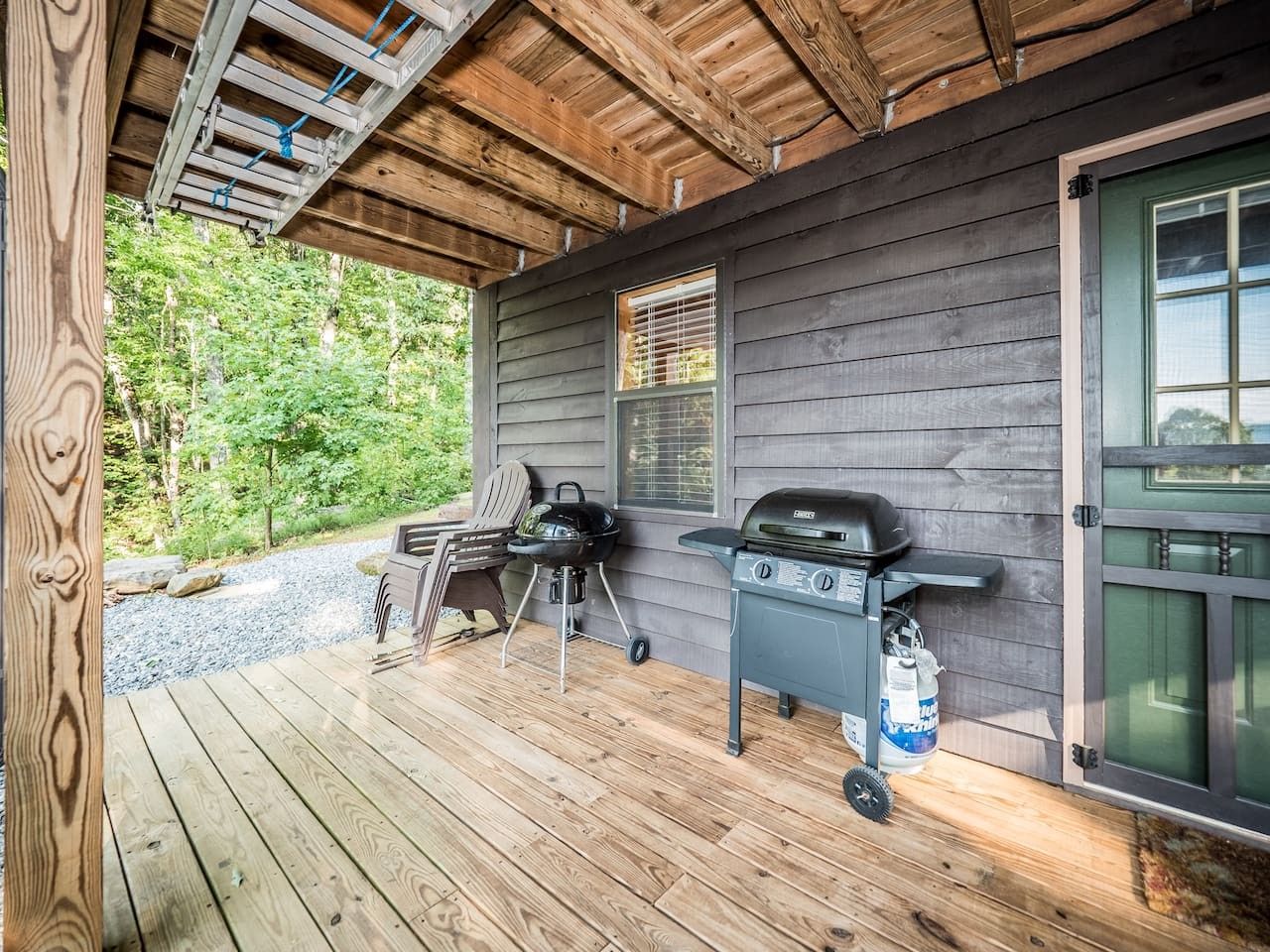 A covered outdoor area with a grill and a chair, a wooden deck, and a door with a window.
