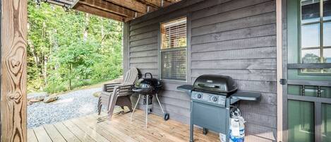 A covered outdoor area with a grill and a chair, a wooden deck, and a door with a window.