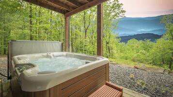 A hot tub on a wooden deck with a view of a forest and mountains.