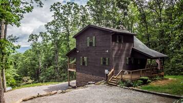 A two-story wooden cabin with a porch, surrounded by trees.