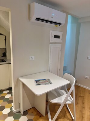 A small room with a white table, a white chair, a white air conditioning unit, and a hexagonal patterned floor. - CASA PICICIO ASSISI (Assisi)