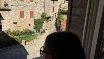 Un edificio in pietra con una stretta via che vi conduce, cielo sereno e una persona seduta su un balcone.