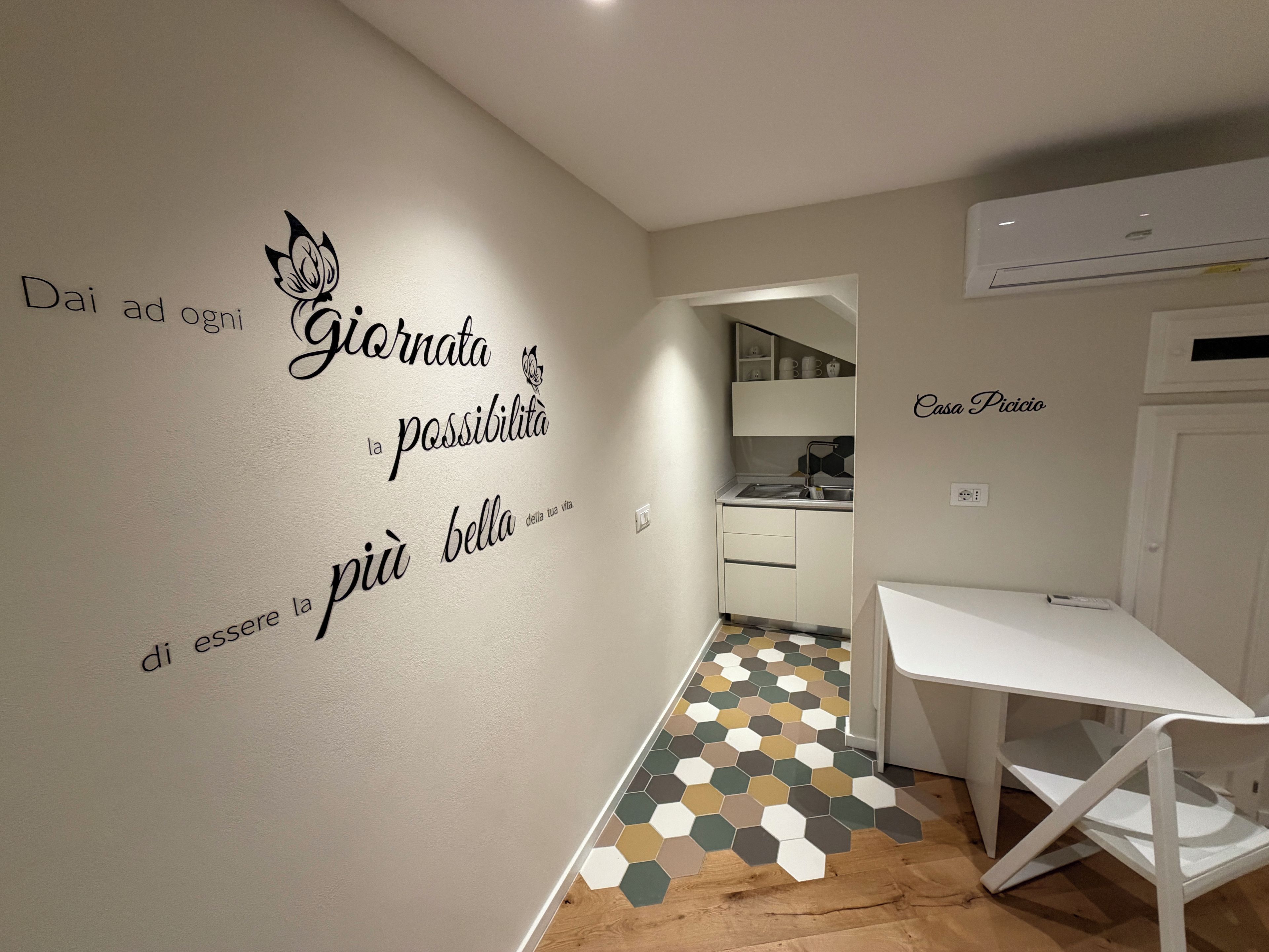 Una cucina moderna con un piano di lavoro bianco, un pavimento a motivi esagonali e una parete con citazioni motivazionali in italiano.