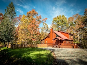 Une cabane en bois avec un toit en pente, entourée d’une clôture en bois et d’arbres aux feuilles d’automne.