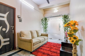 A modern hotel lobby with a beige sofa, a red rug, and a vase of sunflowers. - Super Hotel O Jessore Road Kolkata (Barakpur)