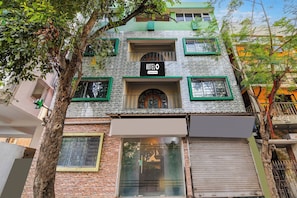 A building with a sign indicating it is a hotel, featuring a stone facade, multiple windows with green frames, and a visible entrance. - Super Hotel O Jessore Road Kolkata (Barakpur)