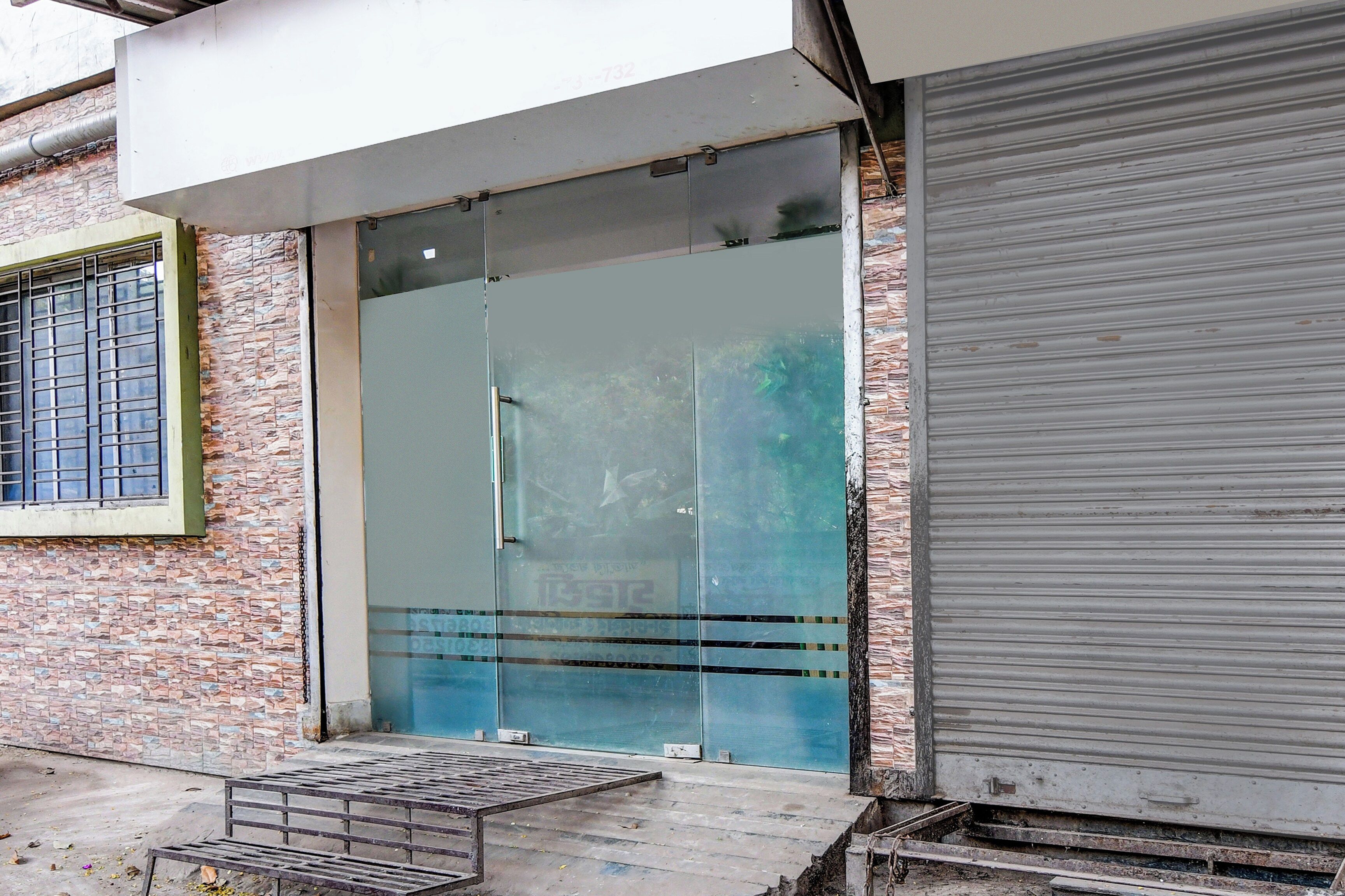 Entrada de edifício com porta de vidro, escada de metal e parede de tijolos.