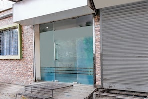 Entrada de un edificio con puerta de vidrio, escalera de metal y pared de ladrillo.