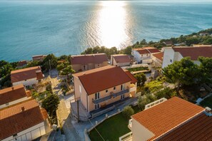 A coastal residential area with houses featuring red-tiled roofs and a view of the sea. - Apartments Palma - Two Bedroom Apartment With Balcony and Sea View (Omis)