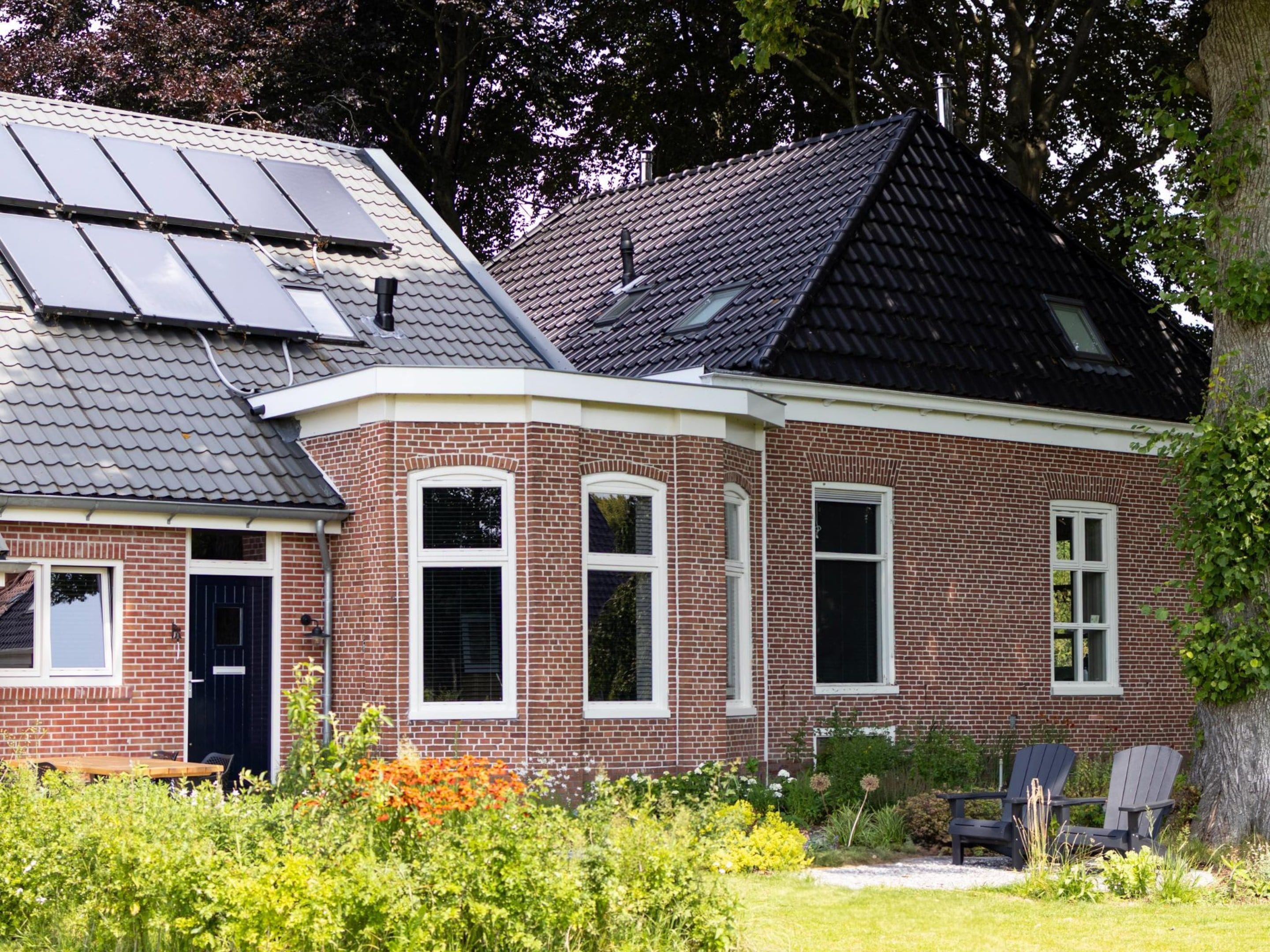 Une maison en briques avec un toit en pente, des panneaux solaires et un jardin agrémenté de fleurs et de plantes.