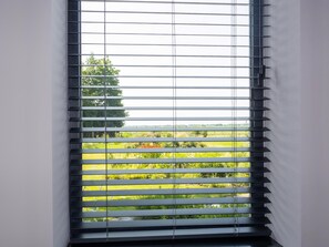A window with horizontal blinds, through which a green landscape is visible. - Charming Holiday Home in Kiel-windeweer (Kiel-Windeweer)