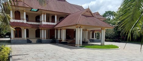 A large building with a tiled roof and multiple columns, surrounded by a paved courtyard.