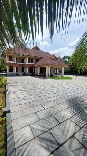 A large building with a tiled roof and multiple columns, surrounded by a paved courtyard.