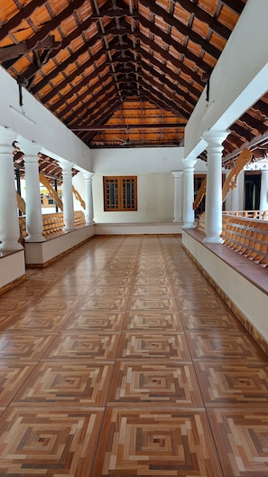 A spacious corridor with a patterned wooden floor, white columns, and a wooden ceiling.