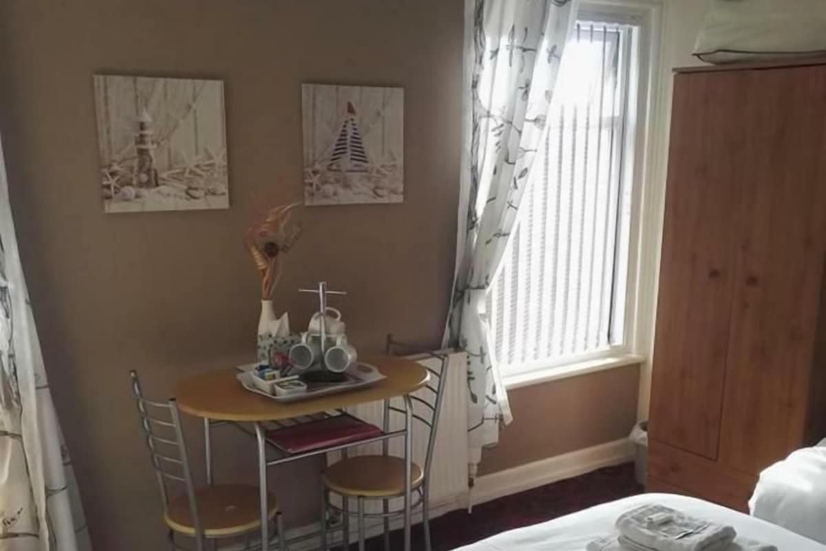 A hotel room with a bed, a desk with chairs, a window with curtains, and artwork on the wall.