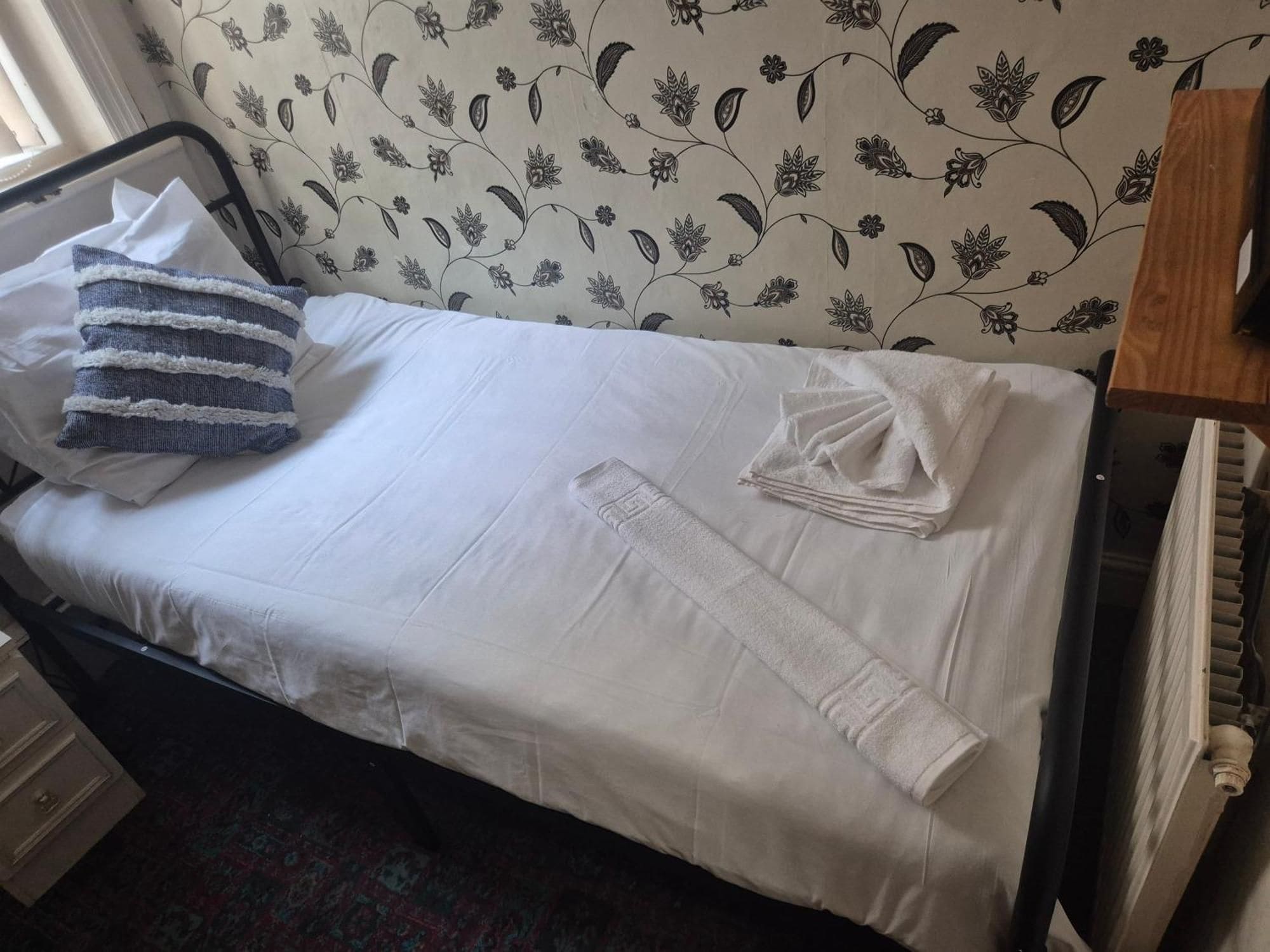 Una cama con sábanas blancas, una almohada azul y blanca a rayas y una toalla blanca doblada.