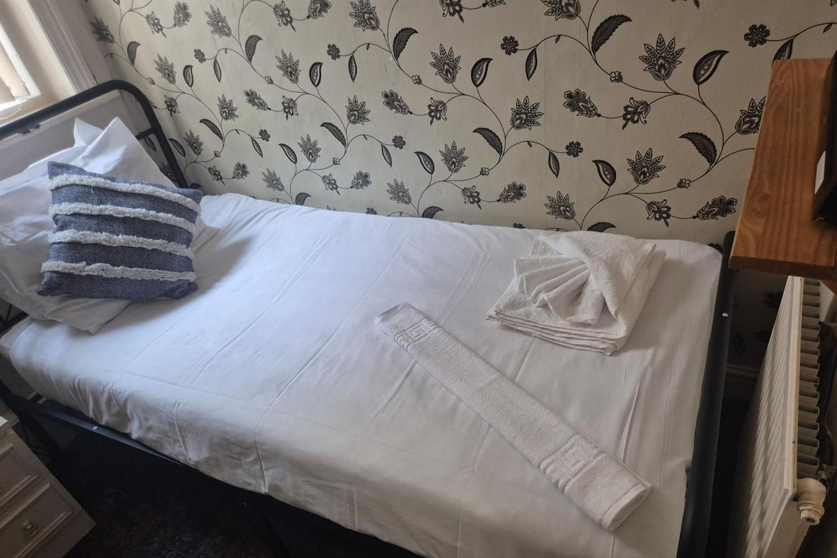 A bed with white linens, a blue and white striped pillow, and a folded white towel.