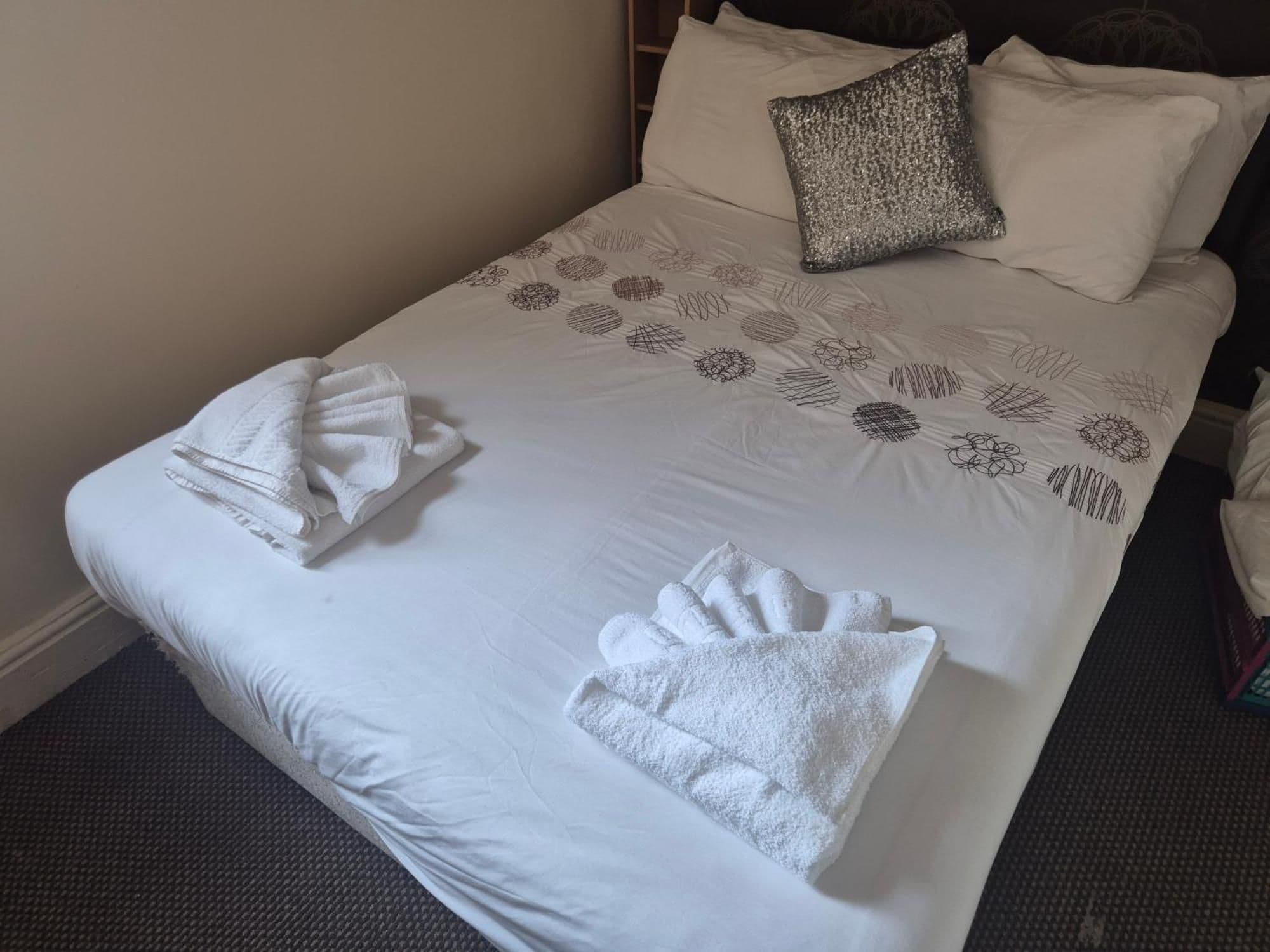 A neatly made bed with a patterned bedspread, two pillows, and folded towels.