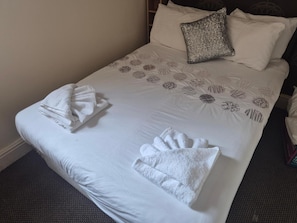 Una cama bien hecha con una colcha estampada, dos almohadas y toallas dobladas.