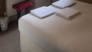 A hotel room with a bed, a desk with a computer, a radiator, and a window with blinds. - White Moon Hotel (Blackpool)