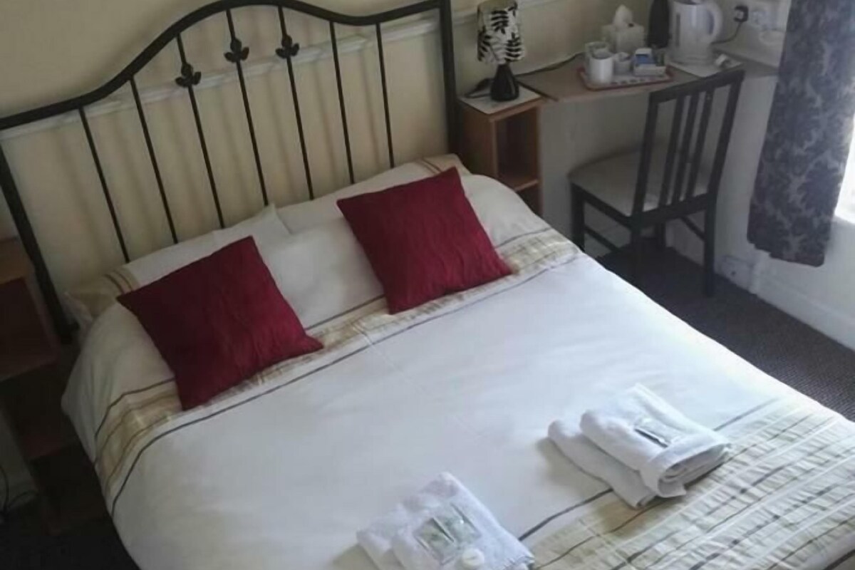 A neatly made bed with a striped bedspread, two red pillows, and a set of folded towels on the bed.