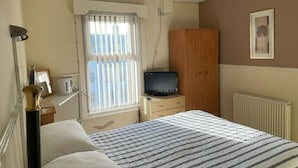 A bedroom with a bed, a wooden wardrobe, a television, and a window with blinds. - White Moon Hotel (Blackpool)
