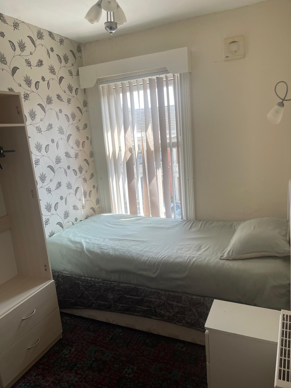 A bedroom with a bed, a wardrobe, a radiator, and a window with curtains.