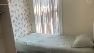 A bedroom with a bed, a wardrobe, a radiator, and a window with curtains.