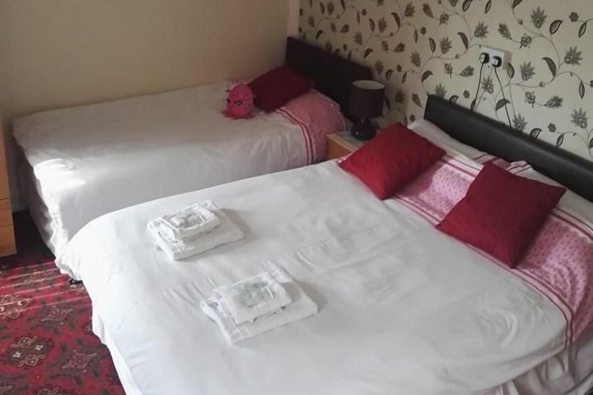 A hotel room with two beds, each with white bedding and red pillows. There are towels folded on the beds.