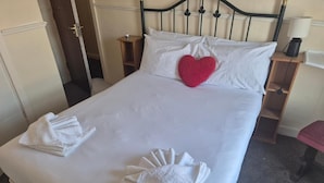 A neatly made bed with white linens, a red heart-shaped pillow, and folded towels on the bed. - White Moon Hotel (Blackpool)