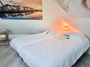 A bedroom with a bed, a chair, a wall-mounted lamp, and a cityscape painting. - Mb02 Holiday Home The Little Fox (Middelburg)