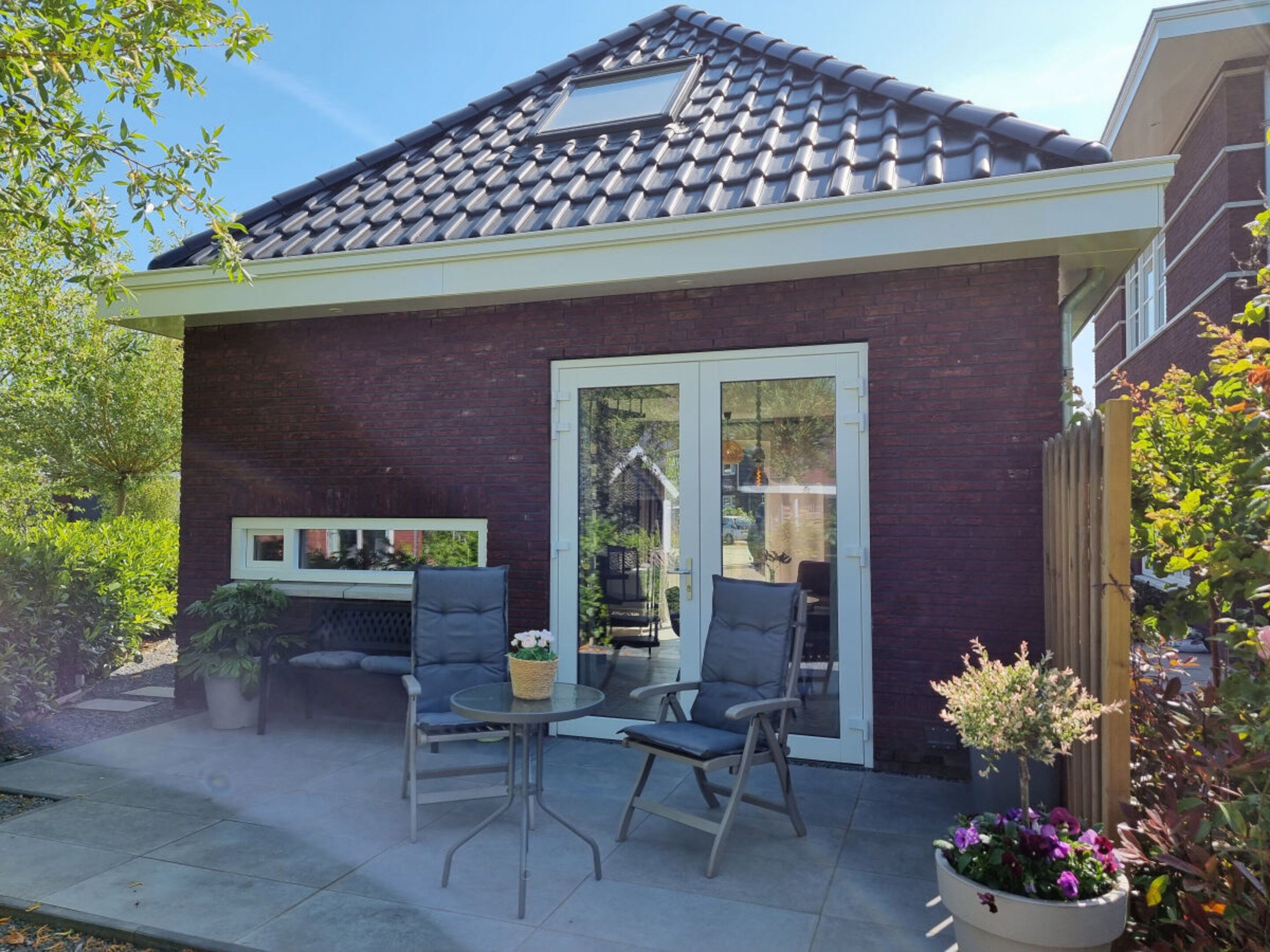 A house with a tiled roof, a brick exterior, and a patio area with two chairs and a table.