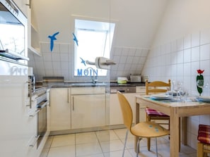 A kitchen with white cabinets, a window with a view, a dining table with chairs, and a red tulip decoration. - 9 in the Thomsen House (St. Peter-Ording)