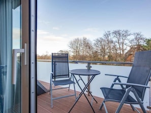 A balcony with two chairs and a table, overlooking a body of water and trees. - 9 in the Thomsen House (St. Peter-Ording)