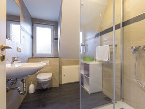 A modern bathroom with a glass shower enclosure, a sink, a toilet, and a window providing natural light. - 9 in the Thomsen House (St. Peter-Ording)