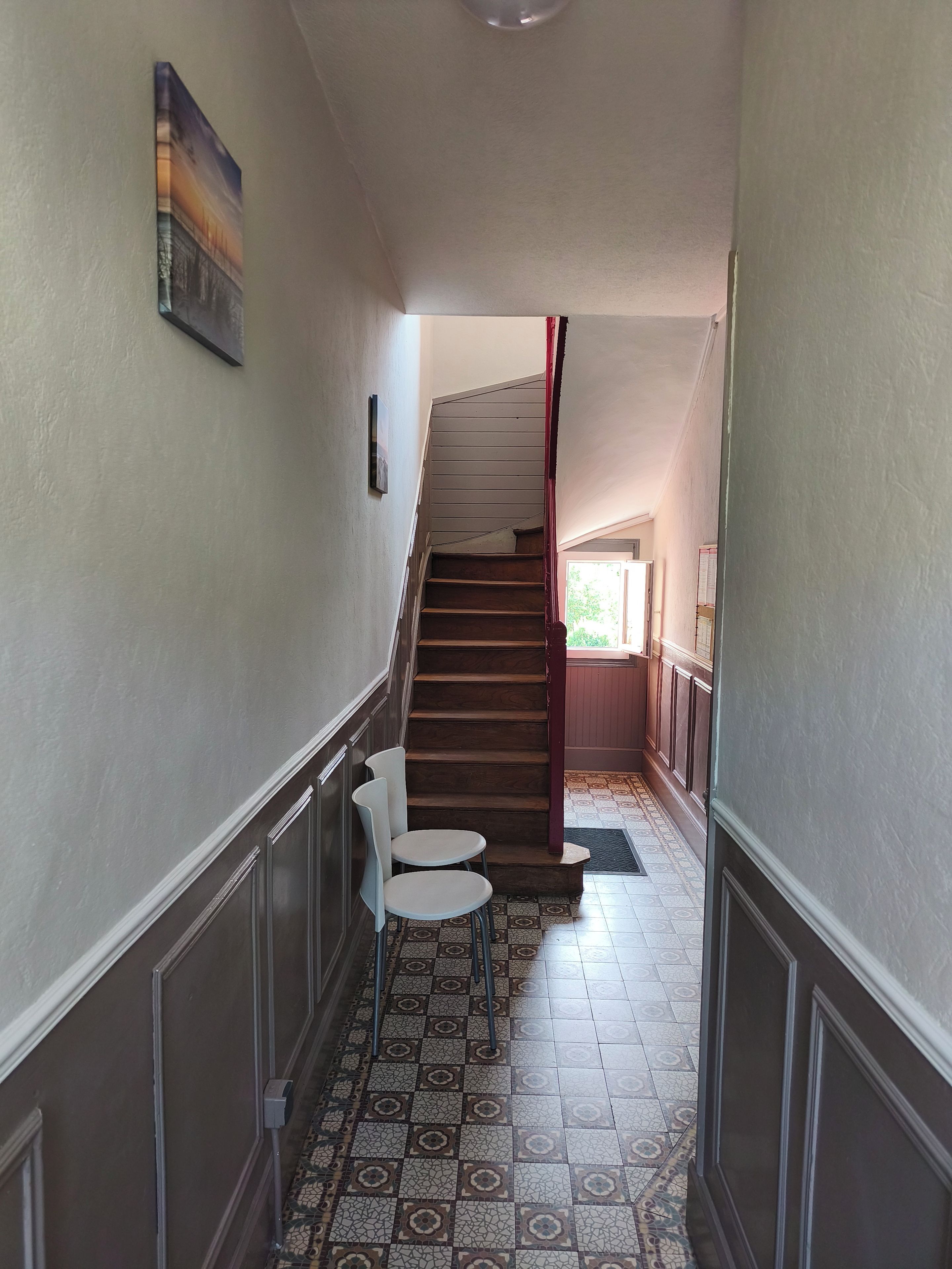Un couloir avec un revêtement de sol à motifs, un escalier et deux chaises blanches.