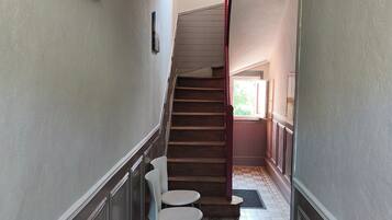 Un couloir avec un revêtement de sol à motifs, un escalier et deux chaises blanches.